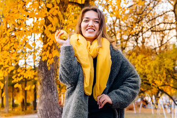 A young woman in a gray coat and yellow scarf holds a lemon fruit vitamin C concentrate in her hands. The concept of happiness and joy