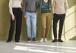 © Studio Romantic - People's legs, cropped indoor low section group shot. Four employees of different sexes and genders in pants and casual jeans standing on office floor against wall background. Work dress code concept