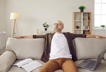 Exhausted middle-aged man relax rest on sofa in living room have break from computer distant job. Tired male sleep on couch distracted from laptop work, need relaxation. Fatigue, overwork concept.