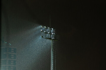 Glowing stadium spotlight at night in rainy weather, copy space