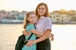 Outdoor portrait of mom and daughter 10, 11 years old on the sunset city sea promenade