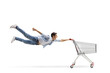 Leinwandbild Motiv Full length shot of a casual guy man flying and holding an empty shopping cart