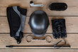 Black set of equipment for horse care and riding: helmet, whip, gloves, bridle, brushes on the wooden background