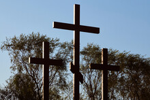 Silhouette Of Three Crosses At Sunrise, Blue Sky And Green Trees Background