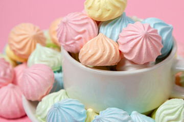 Wall Mural - Multicolored meringues on a pink background. A teacup overflowing with colored meringues.