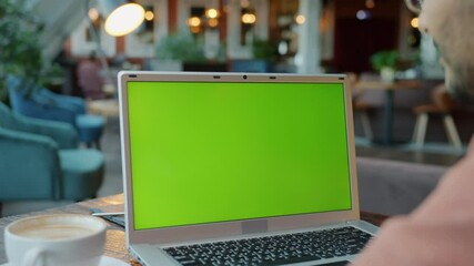 Slow motion of man looking at chroma key green screen laptop at table in cafe. Avertisement content and modern technology concept.