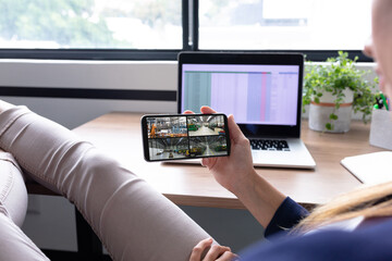 Poster - Caucasian woman holding smartphone with view of warehouse security cameras on screen