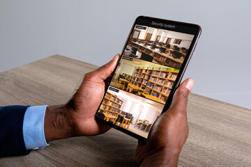 Canvas Print - Hands of african american man holding tablet with view of library from security cameras on screen