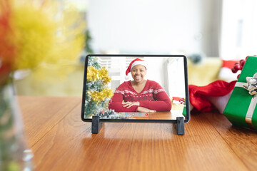 Wall Mural - Smiling african american woman in santa hat on tablet video call screen at christmas