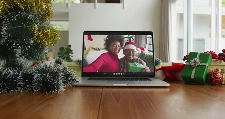 Wall Mural - Smiling african american mother and daughter wearing santa hats on christmas video call on laptop