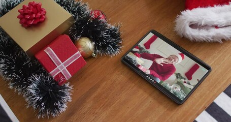 Poster - Smiling albino african american man wearing santa hat and waving on christmas video call on tablet