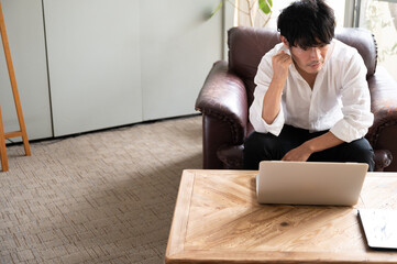 A handsome asian man thinking while working on his computer.