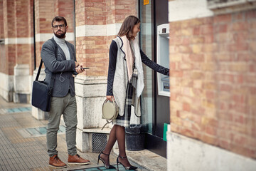 Wall Mural - A young elegant man is nervous while waiting in a row for cash machine since he is late. Walk, ATM, city