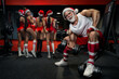 Muscular handsome sexy Santa Claus. Muscular Bodybuilder Guy Doing Exercises With Dumbbells Over in the gym and Girls looking at the mirror