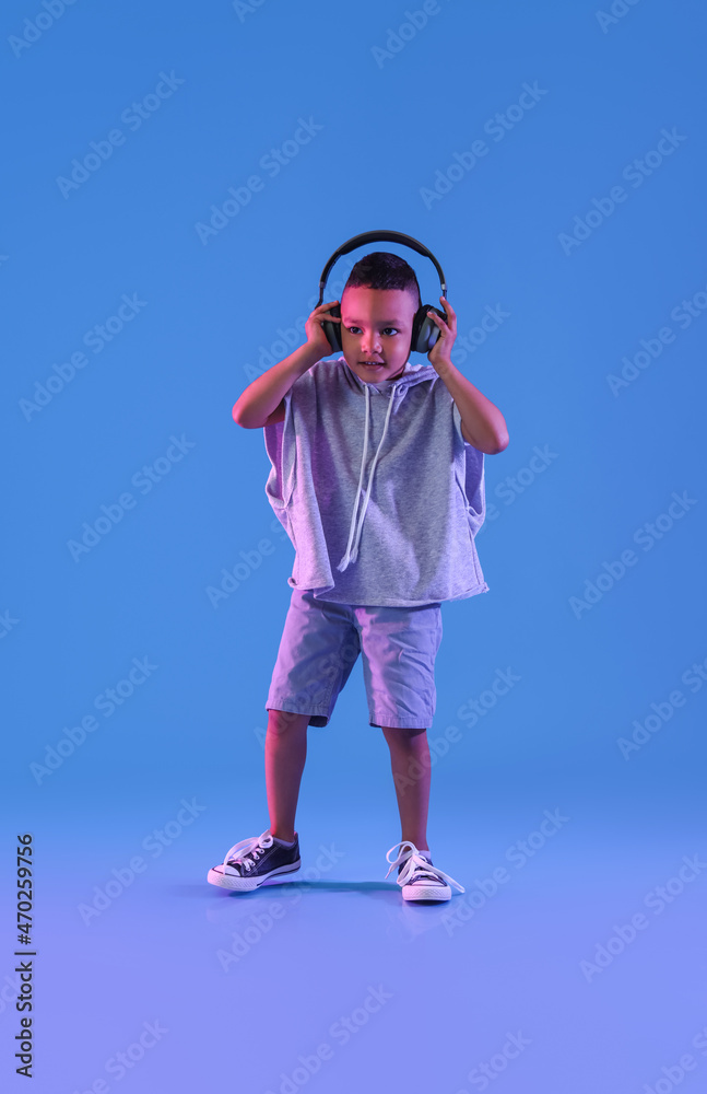 Cute dancing African-American boy with headphones on color background