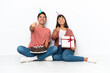 © luismolinero - Young mixed race couple celebrating a birthday sitting on the floor isolated on white background pointing with finger at someone and laughing a lot