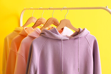 Rack with modern hoodies on color background