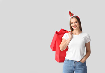 Wall Mural - Beautiful young woman with Christmas decor and shopping bags on grey background