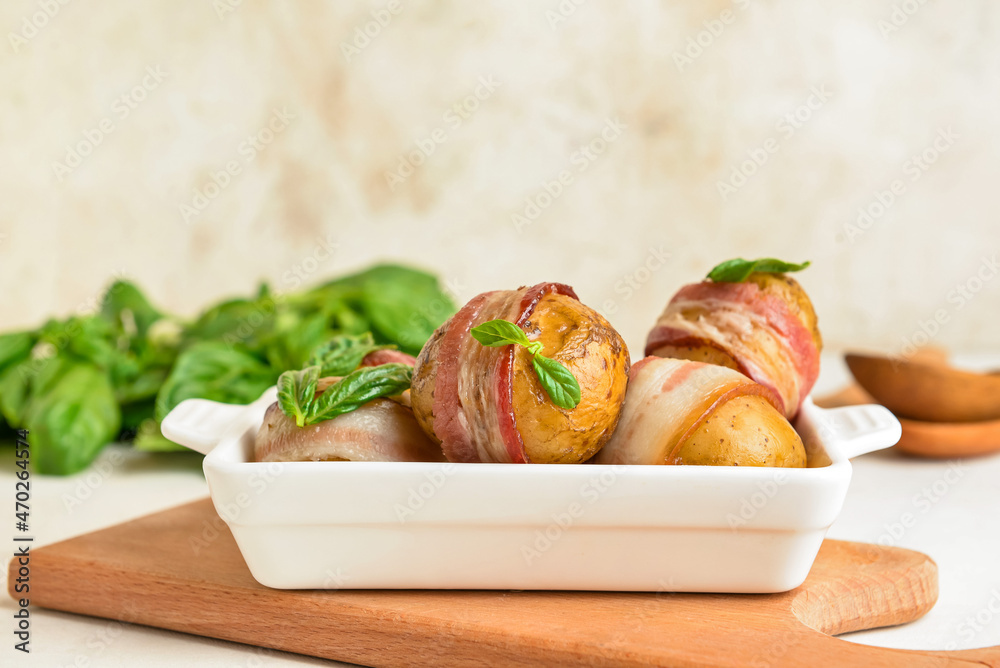 Baking dish of tasty baked potatoes with bacon on light background