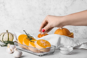 Wall Mural - Woman adding salt in baking dish with fresh pumpkin pieces on light background