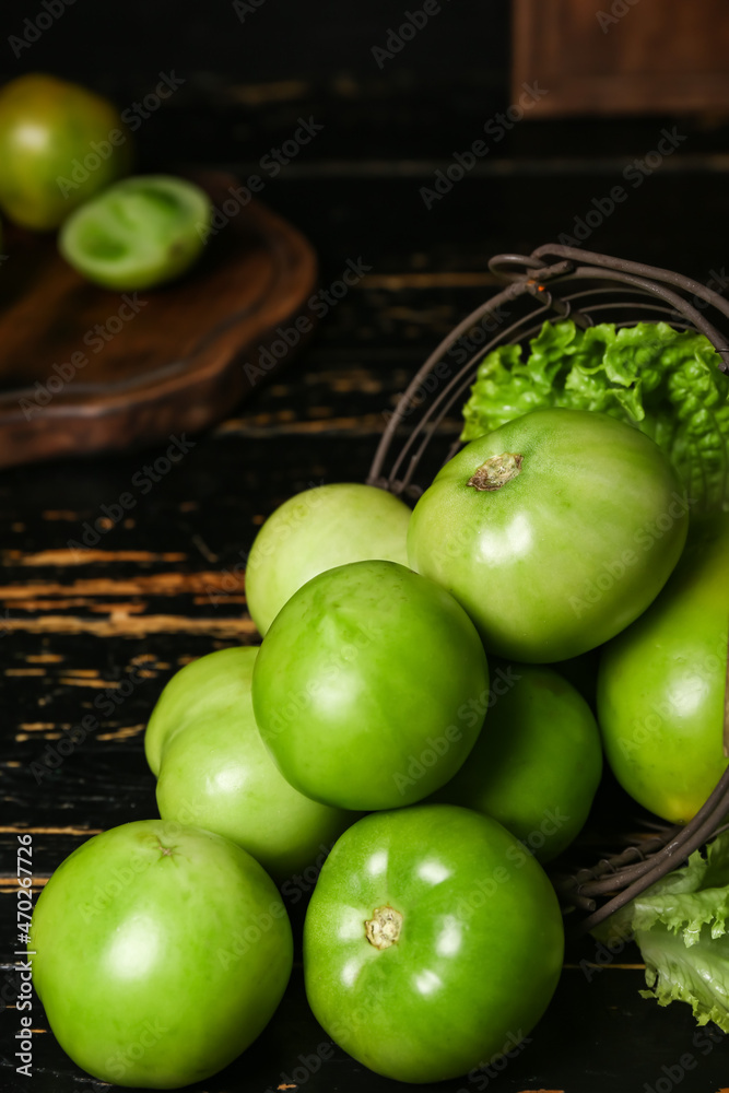 Basket with green tomatoes on dark wooden background, closeup