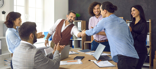 Wall Mural - Two happy people making deal and exchanging handshake in business meeting. Group of smiling office employees applauding as mature man shakes hands with coworker thanking him for achieving good results