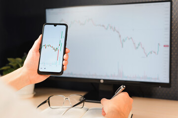 Businessman trader investor analyzing stock market, cryptocurrency, index growth graph, profit and loss in mobile application at workplace, close-up. Business and finance, investment and technology