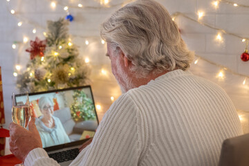 Rear view of senior man in video call with laptop computer celebrating Christmas with a glass of sparkling wine. Happy new year and merry Christmas