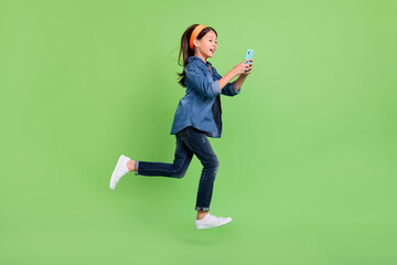 Wall Mural - Full body profile photo of sweet little girl run hold telephone wear hoop jeans sneakers isolated on green color background