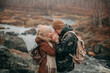 A couple in love in autumn stands on a mountain overlooking the river and forest. The man warms the girl's hands and looks at each other