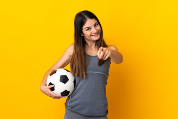 Young football player woman isolated on yellow background pointing front with happy expression