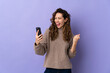 Young caucasian woman isolated on purple background with phone in victory position