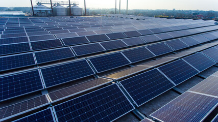 Solar panels mounted on building roof for producing clean ecological electricity. Big cisterns and few engineers at the backdrop. Village landscape on the horizon.