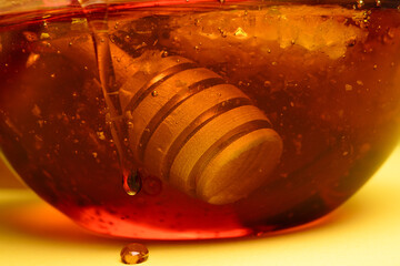 Wall Mural - Wooden stick for honey in a glass jar of fresh liquid honey. Honey dipper closeup.