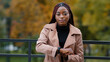 © Yuliia - Running out of time, hurry, to be late concept. Young woman shows on watch, counting minutes, rushing. Portrait of beautiful african american girl with afro hairstyle standing in autumn park alone