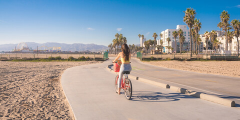 Attractive young woman riding bike near beach with palm trees, Santa Monica, Los Angeles, California