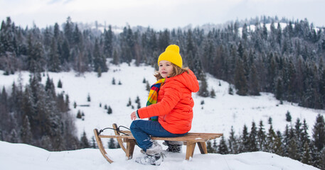 Wall Mural - Funny boy having fun with a sleigh in winter. Cute children playing in a snow on snowy nature landscape. Winter activities for kids.