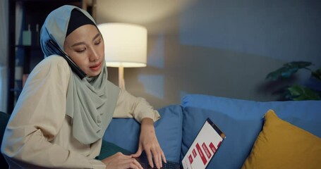 Sticker - Attractive cheerful young Asia muslim beauty woman in hijab with casual sitting on sofa use laptop phone call colleague work on cozy living room in home at night. Girl Islam lifestyle concept.