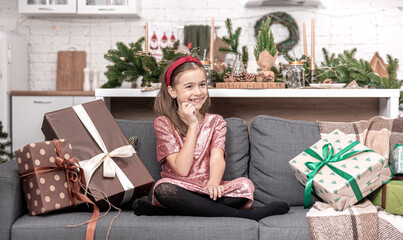 Wall Mural - A little girl enjoys a lot of Christmas gifts sitting on the couch at home.