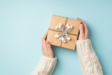 Wall Mural - First person top view photo of female hands in white sweater demonstrating kraft paper gift box decorated with snow twig and twine on isolated pastel blue background