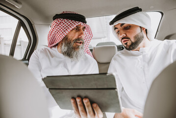 Wall Mural - Senior and young arabian men wearing kandura traditional dress from uae in Dubai. Speaking about business plans