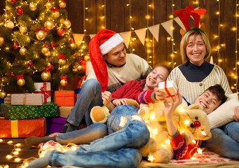 Wall Mural - Family posing in new year or christmas decoration. Children and parents. Holiday lights and gifts, Christmas tree decorated with toys.