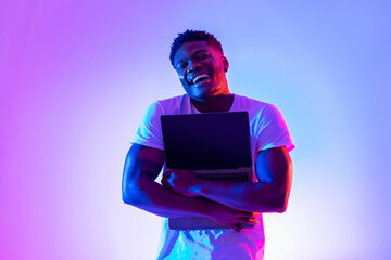 Poster - Technology lover concept. Happy black man hugging laptop with blank screen in neon light, mockup for website design