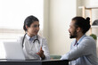 © fizkes - Smiling Indian woman doctor consulting African American man patient, therapist practitioner giving recommendation, discussing checkup results or symptoms at meeting, sitting at desk with laptop