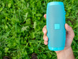 © Sergey - Close-up of a man's hand holding a blue wireless music speaker. There is a thick green grass in the background. Using an outdoor device. Top view, Copy space