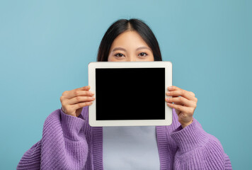 Young asian lady hiding her face behind digital tablet with empty black screen, showing cool mobile application