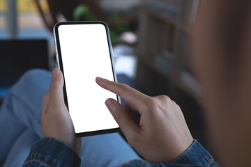 Poster - Cell phone mockup image blank white screen. Woman hand holding, using mobile phone during working on laptop computer at home, over shoulder view