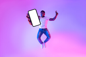 Poster - Full length of excited African American guy jumping with smartphone, demonstrating empty screen in neon light, mockup