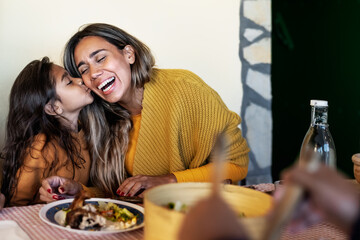 Happy Hispanic mother having tender moment with daughter while dining together with family - Parents love concept