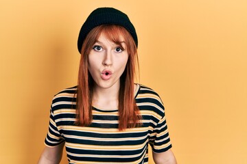 Poster - Redhead young woman wearing wool cap scared and amazed with open mouth for surprise, disbelief face